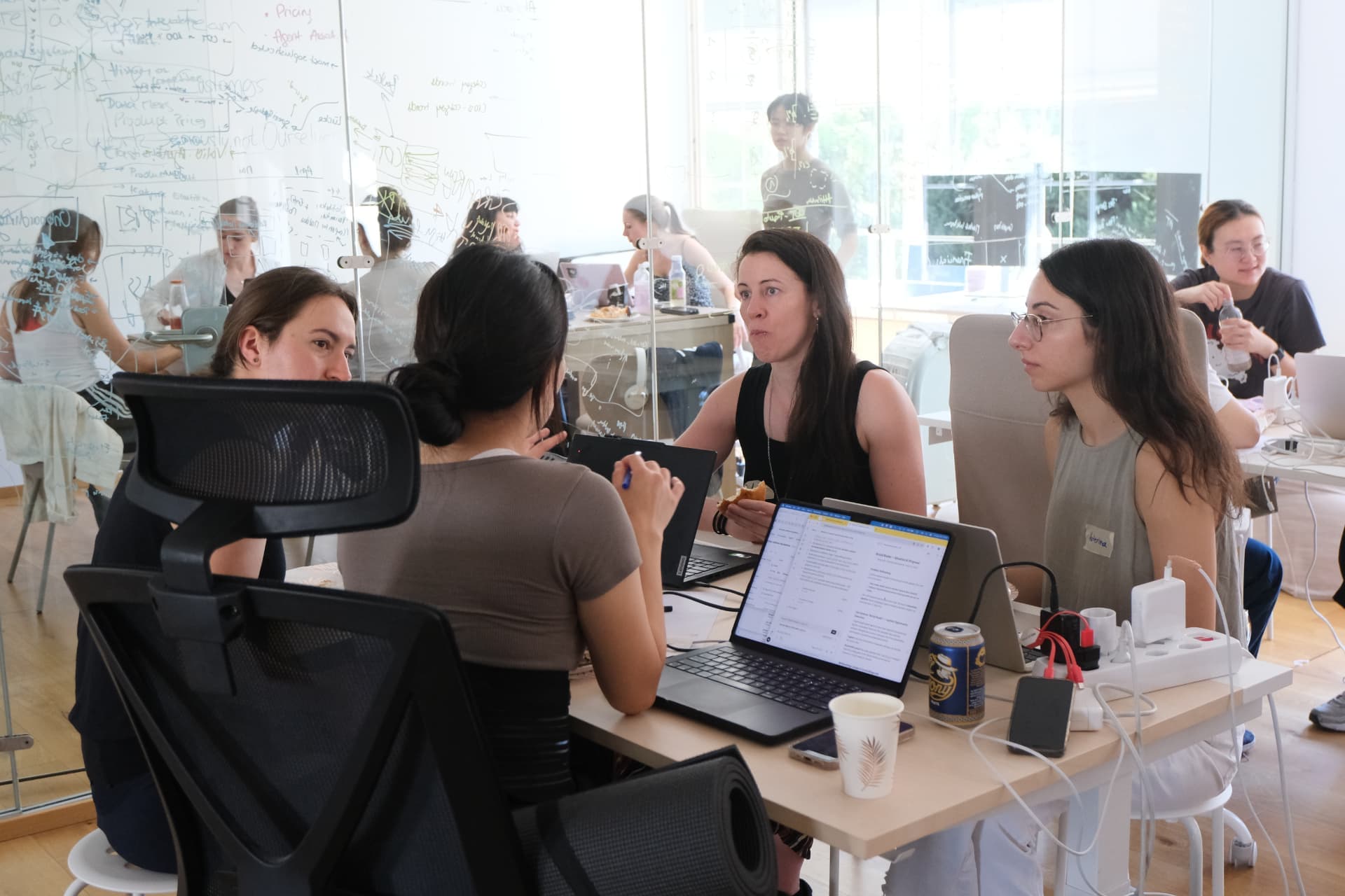 Participants discussing their project behind glass whiteboards at the all-women AI hackathon